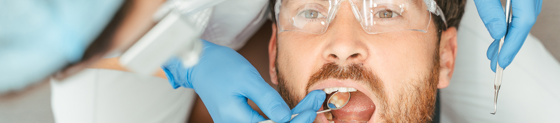 A person is seated in a dental chair, receiving care from a dental professional who stands behind them.